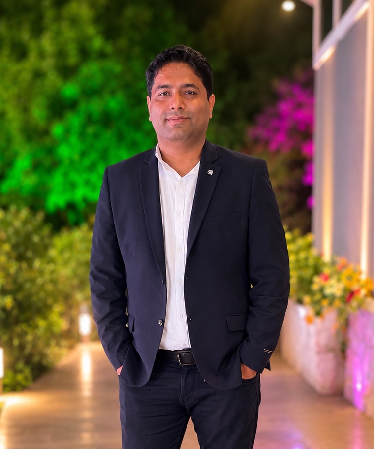 Pushpendra Singh in a navy blazer, standing on a lit garden path
